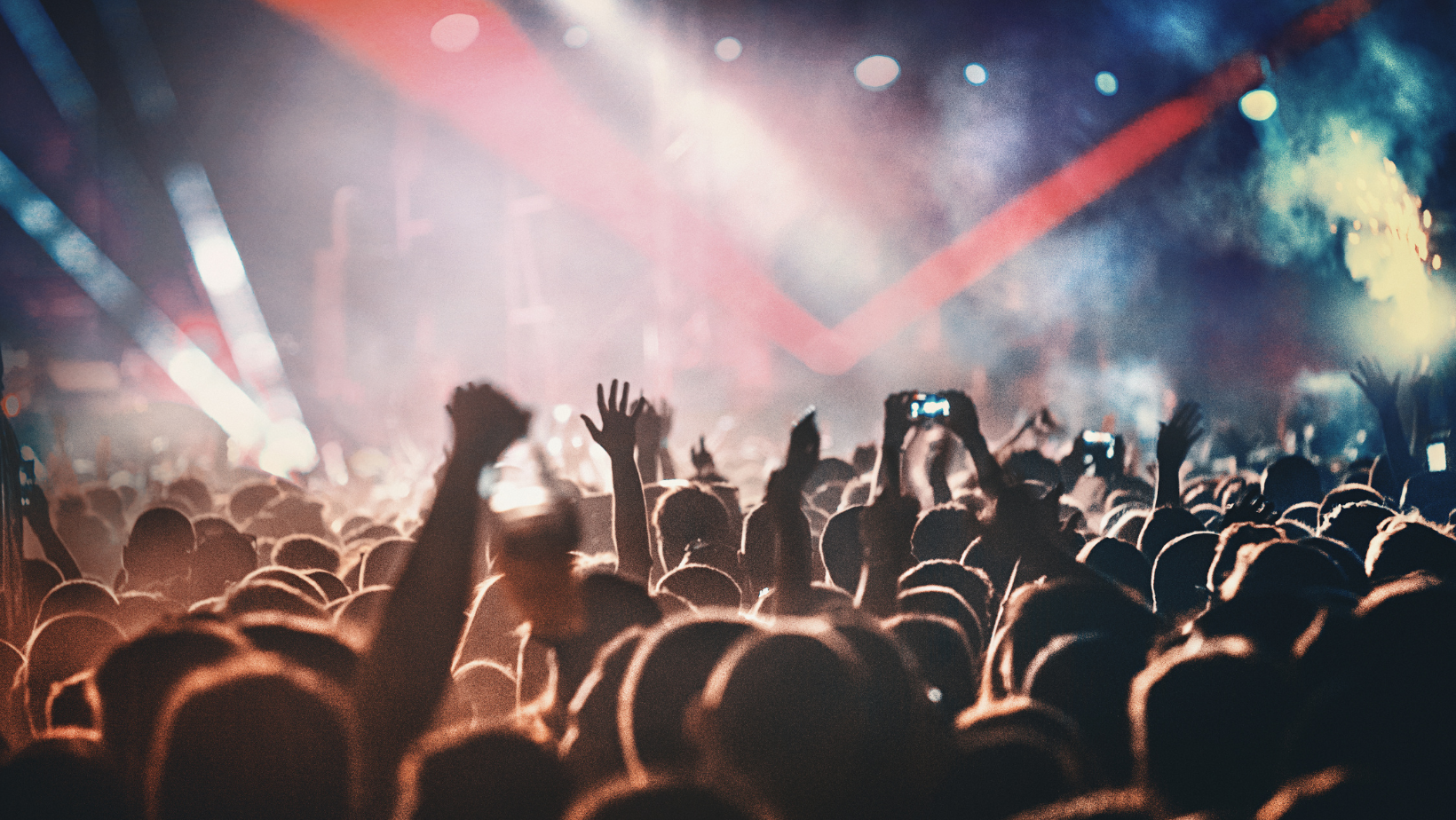 People attending a concert in a large stadium, dark ambience with coloured strobe lights