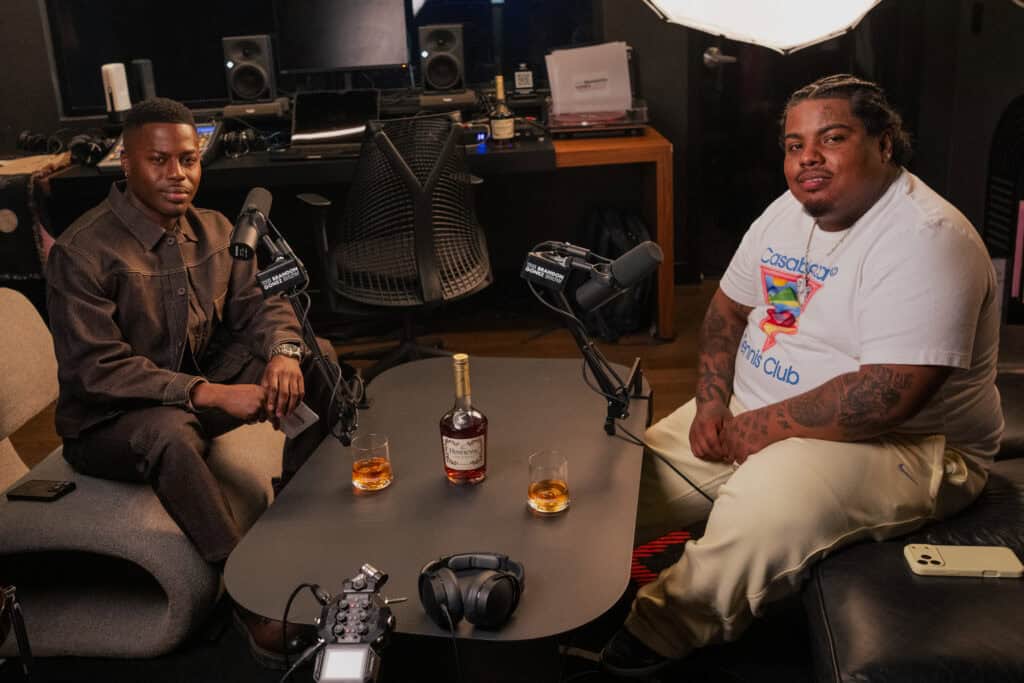 Two men in a podcast studio with microphones and drinks on the table.