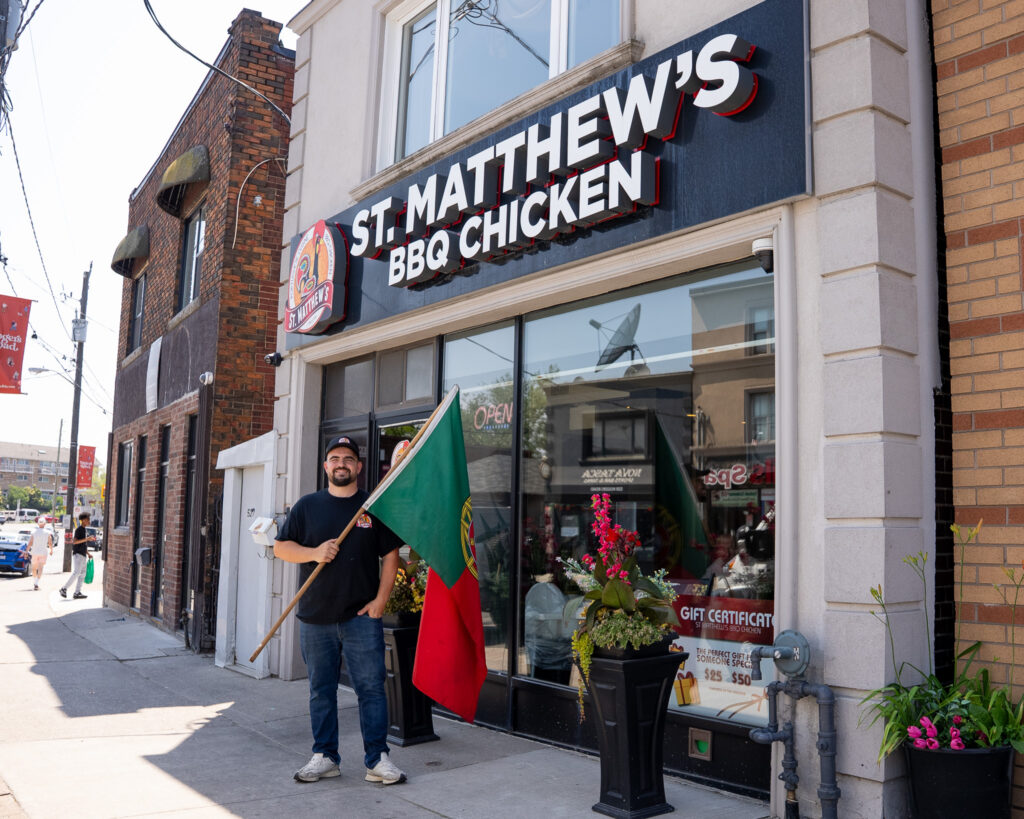 Man holding Portuguese flag outside St. Matthew's BBQ Chicken restaurant in Toronto.